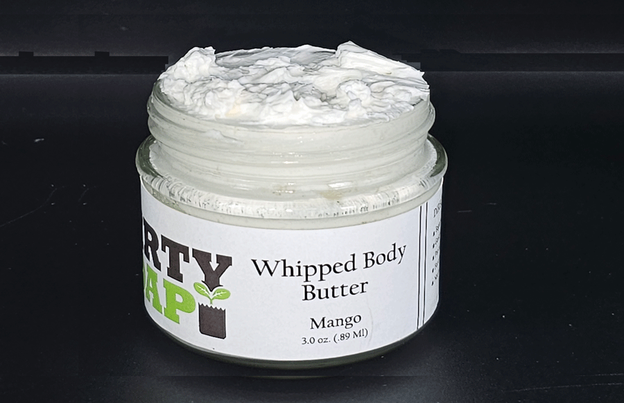 Open jar of Dirty Soap's Mango Whipped Body Butter with mango scent and natural ingredients on a black surface.