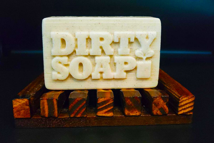 A bar of Eucalyptus and Spearmint Bar Soap labeled "Dirty Soap Bubbles" on a wooden soap dish.