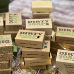 Stacks of handmade soap bars in various scents, labeled "dirty soap" and packaged in brown cardboard boxes.