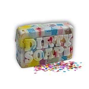 The Dirty Soap Confetti Soap Bar, a rectangular bar featuring colorful confetti pieces and an embossed logo, infused with spearmint essential oil, is shown beside scattered confetti on a white background.