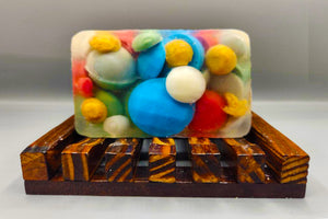 Handcrafted Christmas Rocks bar soap with colorful embedded beads and essential oils on a wooden soap dish by Dirty Soap.