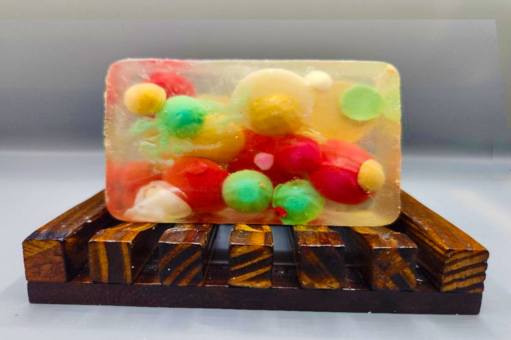 Multicolored gumballs encased in a clear resin block displayed on a wooden stand with a hint of Christmas Rocks Traditional Bar Soap from Dirty Soap.