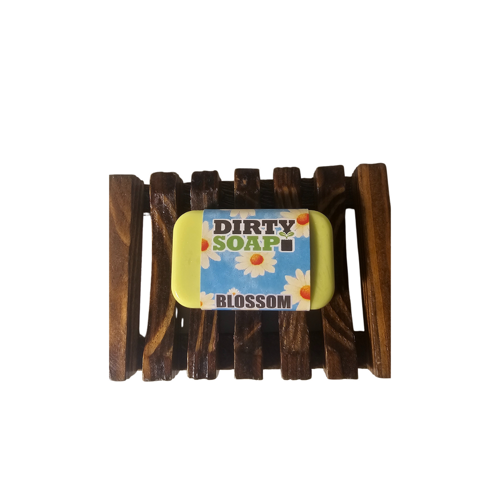 A "Dirty Soap" Mini Bars Sampler Set with floral designs rests on a dark wooden soap dish alongside an exfoliating soap saver bag, all displayed against a white background.