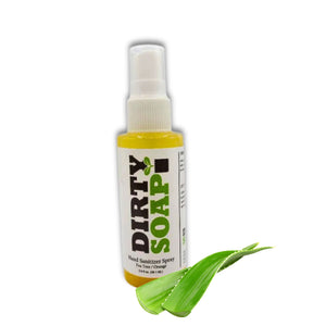 A bottle of Dirty Soap Bubbles Hand Sanitizer spray with ethyl alcohol, tea tree, and orange stands next to two green aloe vera leaves.