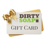 A Dirty Soap Shoppe Gift Card, elegantly adorned with a gold bow and envelope, is the perfect gift for treating someone to luxurious scents and self-care essentials.