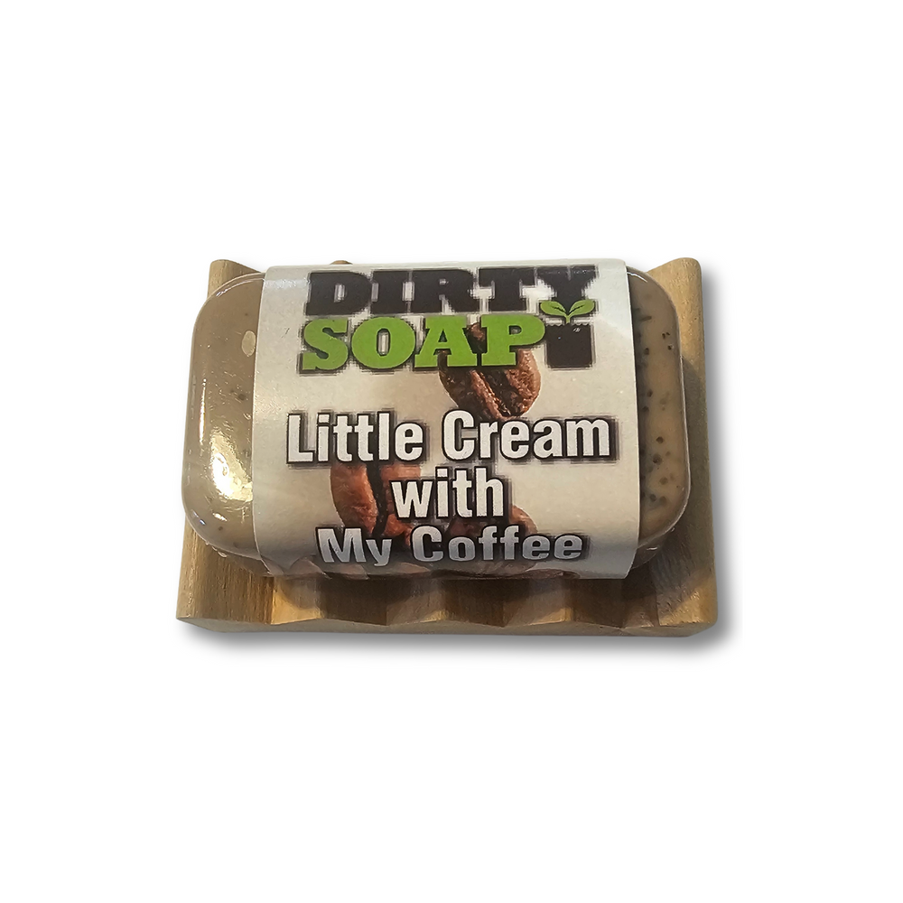 A Dirty Soap Mini Bar by Dirty Soap, labeled "Little Cream with My Coffee" and made from natural ingredients, rests on a small wooden soap dish against a white background.