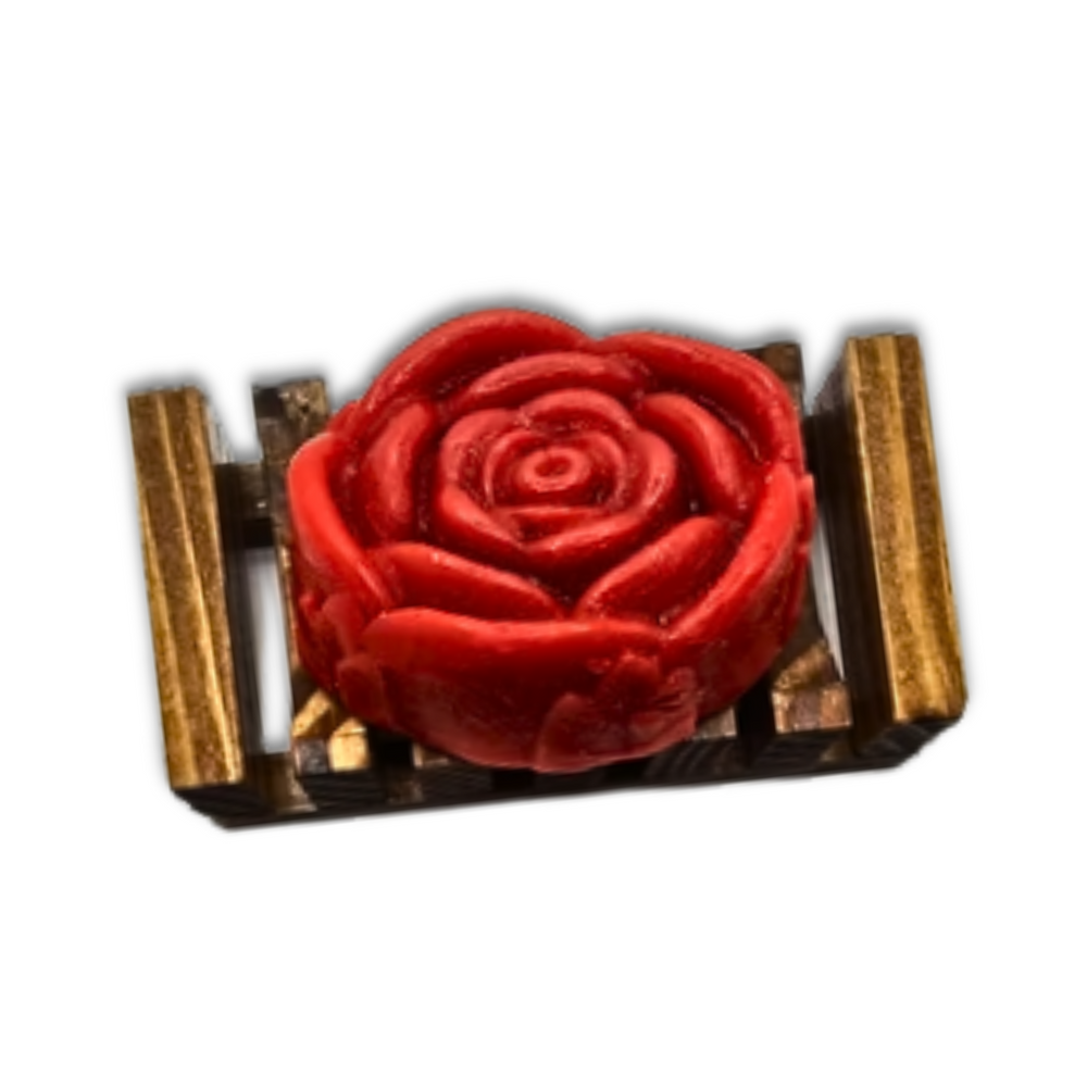 The Dirty Soap Shoppe Red Rose Flower Soap, shaped like a bloom and infused with calming rose essential oil, sits elegantly on a small rectangular gold and brown wooden platform.