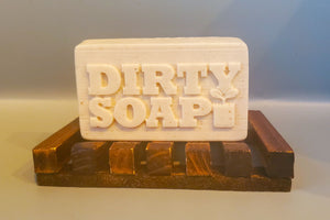 A Mango and Bergamot Bar Soap with the brand "Dirty Soap" embossed on it, resting on a wooden soap dish.