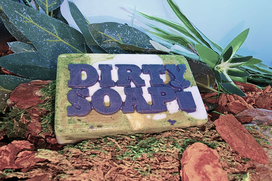 Bar of Open Air Bar Soap by Dirty Soap placed on a natural background with foliage and bark.