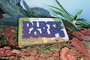 Bar of Open Air Bar Soap by Dirty Soap placed on a natural background with foliage and bark.