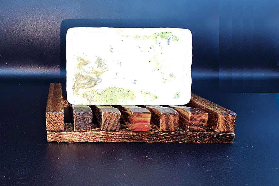 A Dirty Soap Open Air Bar Soap resting on a wooden soap dish with a black background.