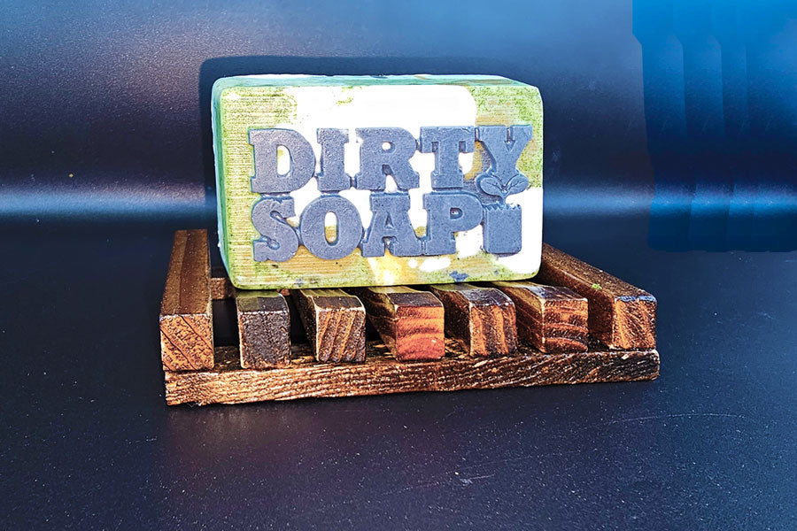 A handmade Open Air bar of soap with the words "Dirty Soap" on a wooden soap dish.