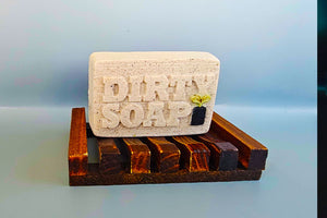 A bar of Dirty Soap's Vanilla And Lavender Bar Soap on a wooden soap dish.