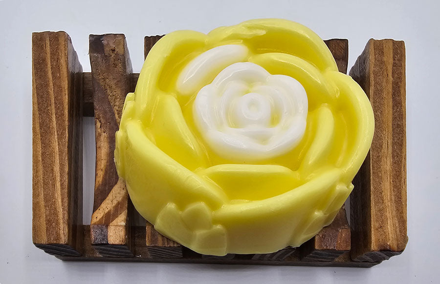 A Yellow Rose Honeysuckle & Jasmine Flower Soap by Dirty Soap Shoppe, sits on a wooden soap dish. Perfect for reducing dark spots & acne while providing stress relief.