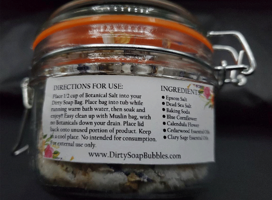 A close-up of a jar of Blue Cornflower and Calendula Flower soap from Dirty Soap with an ingredients label, slightly out of focus.