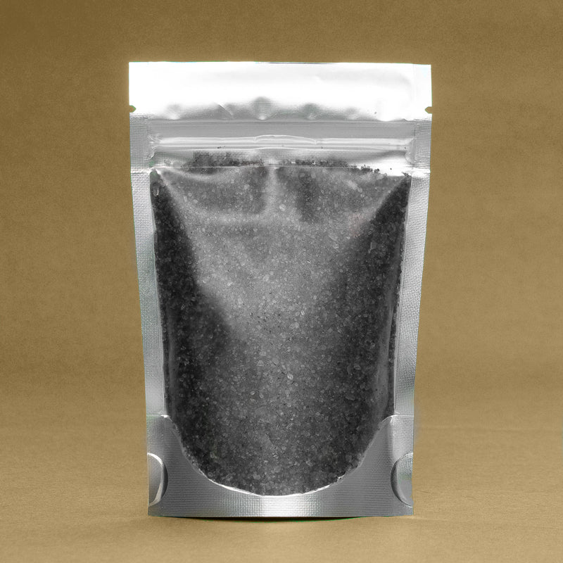 A silver sealed pouch containing Arctic Charcoal & Peppermint Bath Salts by Dirty Soap Bubbles against a brown background.