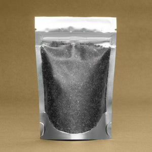 A silver sealed pouch containing Arctic Charcoal & Peppermint Bath Salts by Dirty Soap Bubbles against a brown background.