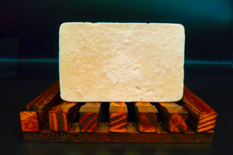 A bar of Dirty Soap Bubbles' Eucalyptus and Spearmint Bar Soap resting on a wooden soap dish.