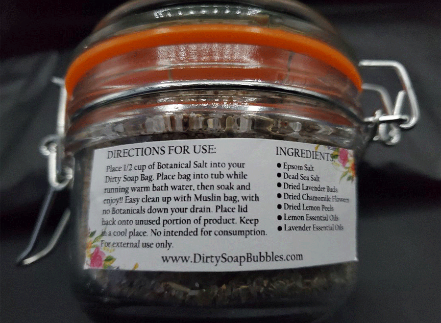 A close-up of a glass jar with a metal clasp, labeled with instructions for use of Dirty Soap's Lemon Lavender Botanical Salt mixture, alongside ingredients listed on the side, including Lavender, Epsom Salt.