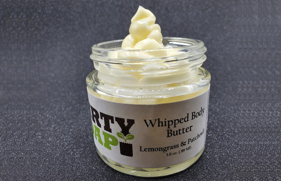 A jar of Lemongrass And Patchouli Whipped Body Butter with a dollop of the Dirty Soap Bubbles product on display, crafted with natural ingredients.