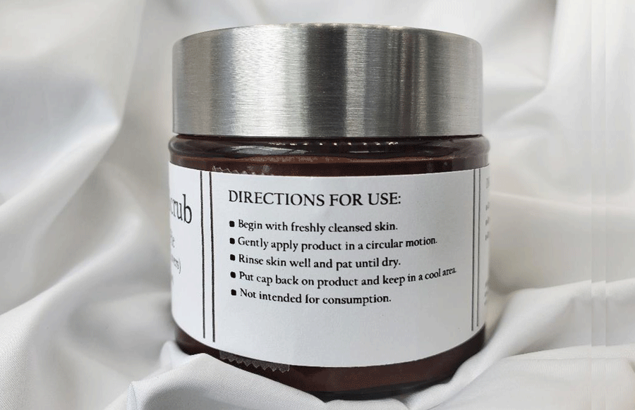 A jar of Dirty Soap Bubbles Mud Pie Sugar Scrub (Chocolate Lovers) with instructions on how to use printed on the label, resting on a draped white fabric.