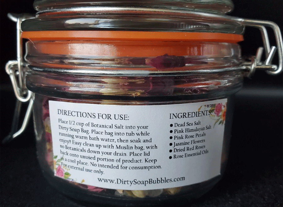 A jar of Wild Rose Botanical Salt from Dirty Soap with a detailed label listing ingredients, including Dead Sea Salt and Rose Essential Oil, and instructions for use.