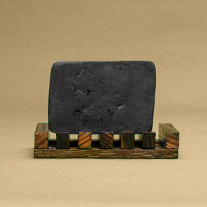 A bar of Dirty Soap's Arctic Charcoal & Peppermint with Goat's Milk Bar Soap resting on a wooden soap dish.