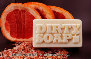 Sliced grapefruit with a Sunrise Grapefruit & Coconut bar of natural, handmade soap labeled "dirty soap" on a bed of Himalayan salt. Brand: Dirty Soap Bubbles.