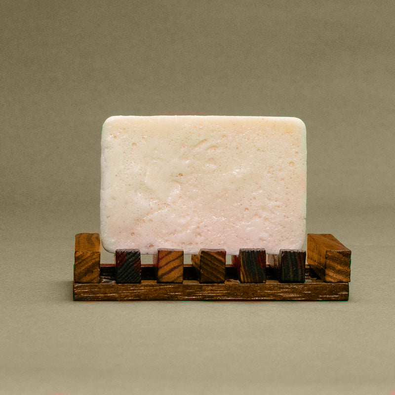 A Sunrise Grapefruit & Coconut with Himalayan Salt bar of soap resting on a wooden soap dish by Dirty Soap Bubbles.