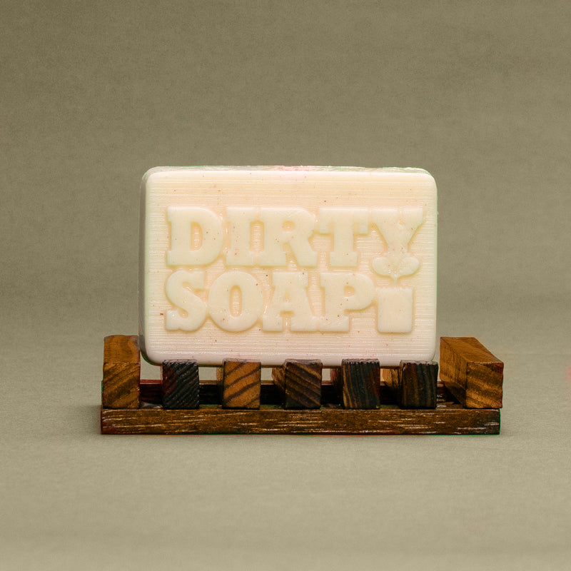 A Sunrise Grapefruit & Coconut with Himalayan Salt bar soap from Dirty Soap Bubbles, with the words "dirty soap" embossed on it, resting on a small wooden pallet.