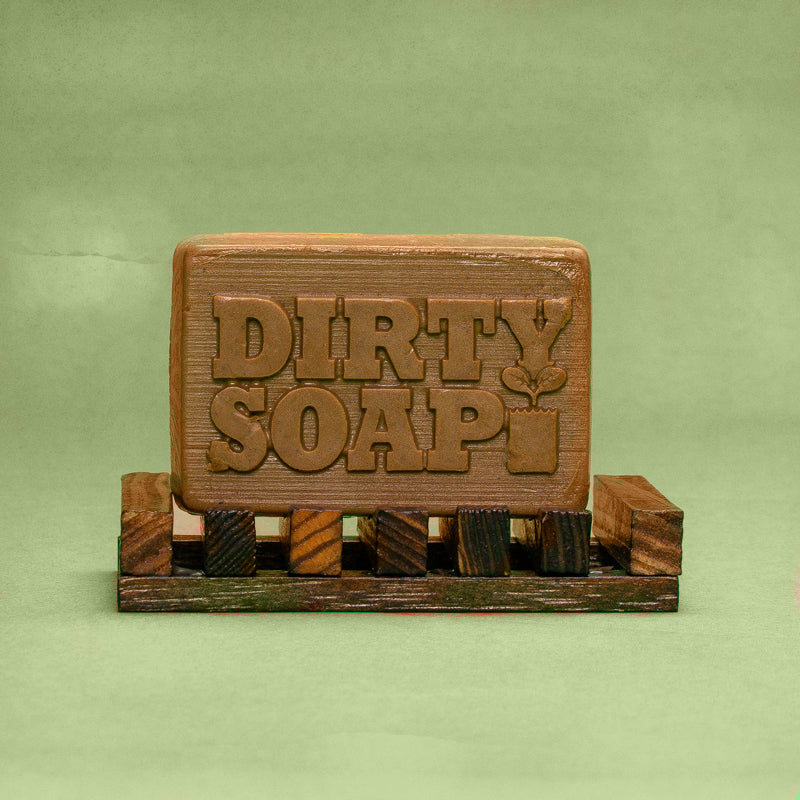 A handmade bar of soap with "Dirty Soap Bubbles" embossed on it, resting on a small wooden pallet against a green background.